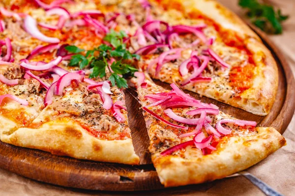 Pizza with tuna and red onion on wooden cutting board. Close up