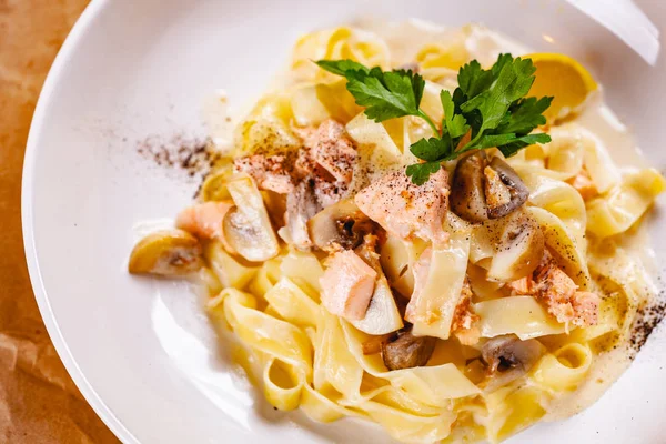Pasta with salmon and mushrooms on white plate. Top view. Close up