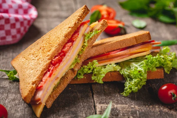 Jambon, peynir, domates ve marul ile sandviç ahşap rustik masada bırakır. Yakın çekim