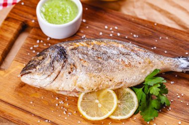 Ahşap tahtada limonlu ve soslu ızgara dorado balığı. Kapat.