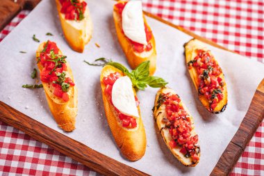 Geleneksel İtalyan bruschetta, kiraz domatesli, fesleğenli ve mozzarella peynirli ahşap kesim tahtasında. Kapat.