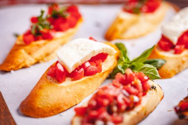 Geleneksel İtalyan bruschetta, kiraz domatesli, fesleğenli ve mozzarella peynirli ahşap kesim tahtasında. Kapat.