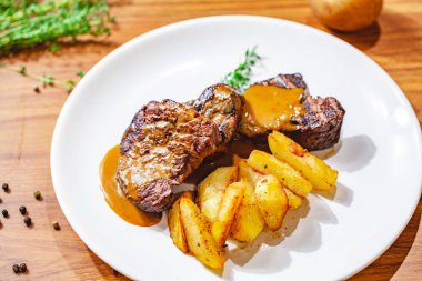 Beyaz tabakta patates dilimli ızgara biftek. Kapat.