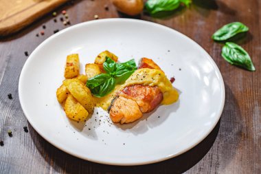Pastırma ve patates dilimleri beyaz plaka üzerinde sarılı ızgara somon fileto. Yakın çekim