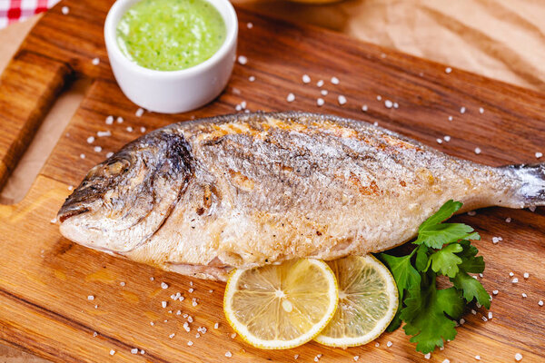 Grilled dorado fish with lemon and sauce on wooden board. Close up
