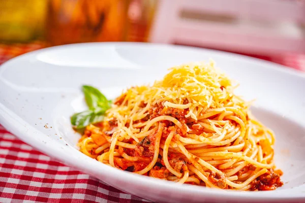 Italian cuisine. Spaghetti bolognese with meat, parmesan cheese and tomatoes on white plate. Close up