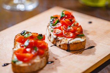 Geleneksel İtalyan bruschetta, kiraz domatesli, peynirli, fesleğenli ve balzamik sirkeli tahta tahtada. Kapat.
