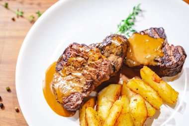 Beyaz tabakta patates dilimli ızgara biftek. Kapat.