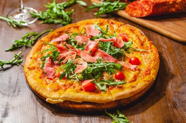 İtalyan pizzası prosciutto (parma jambonu), roka (salata roketi) ve ahşap tahtada vişneli domates. Kapat.