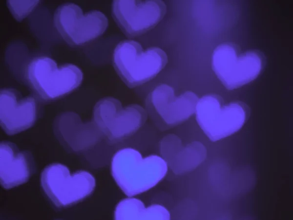Blurred background with bright spots of the bokeh in the shape of a heart. Beautiful background for Valentine\'s day greeting card. Non-standard colors for describing love: lilac, violet, purple, pink