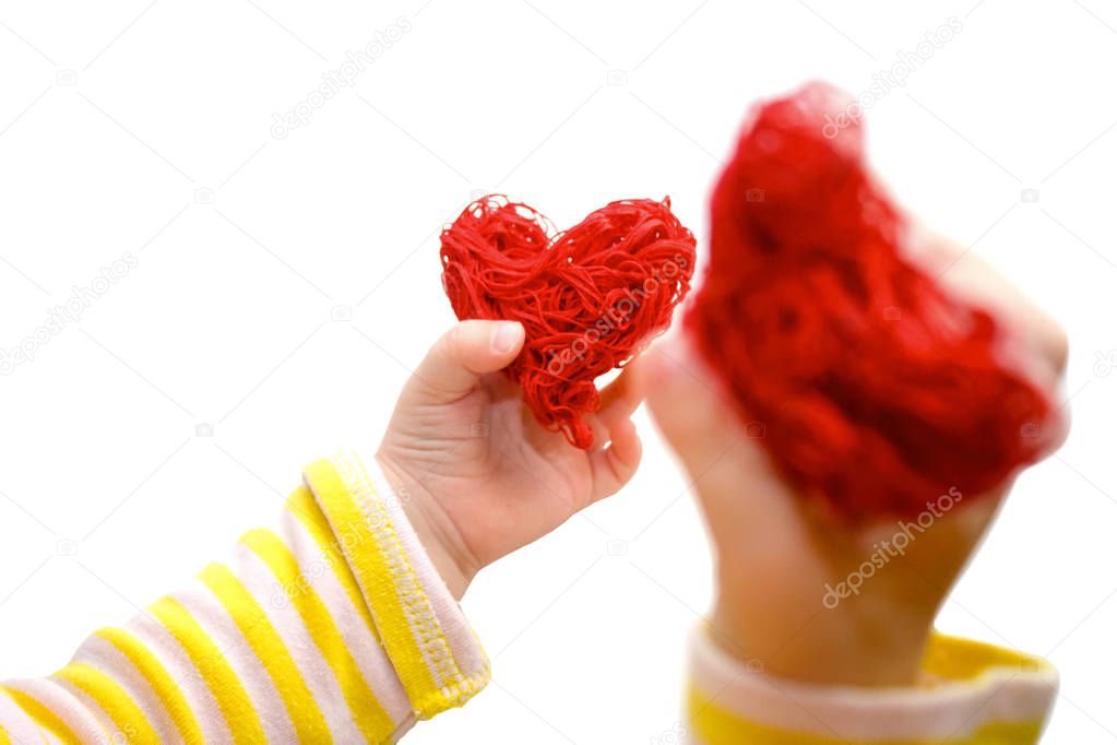 Baby hands holding a red heart. A child plays with red decorative hearts