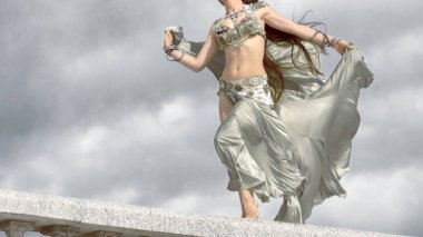 Bir kız oryantal dans için gümüş bir kostüm sonbahar güneş ışınlarının rüzgarda duruyor