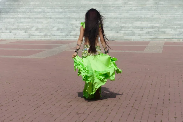 A girl in a traditional oriental costume for belly dancing comes from the viewer. The wind develops her hair and hem dresses.