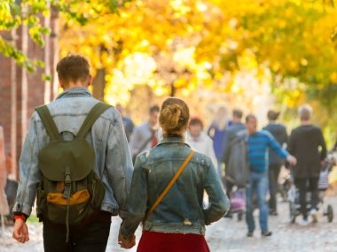 Sonbahar güneşli parkta kalabalığın ortasında yürüyüş aşık genç çift