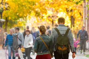 Sonbahar güneşli parkta kalabalığın ortasında yürüyüş aşık genç çift