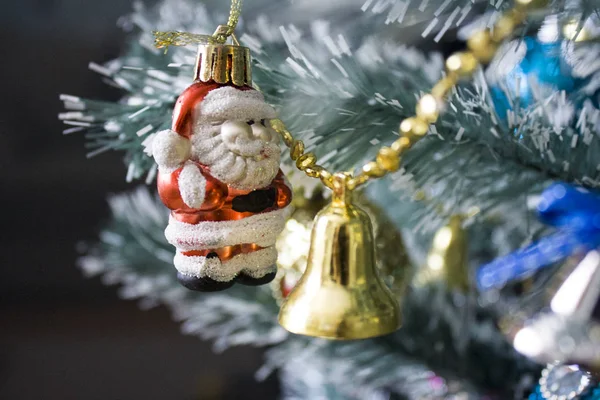 他のおもちゃの隣に人工的なクリスマス ツリーの枝に掛かっている赤と金色のベルのサンタ クロース ロイヤリティフリーのストック写真