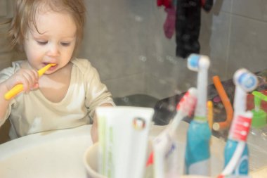 Küçük bir kız çocuğu kirli bir diş macunu sıçramış ayna aracılığıyla görüntüleyin. Çocuk dişlerini fırçalar, ilk süt dişleri kargaşa içinde her şeyin yerini banyoda plak kaldırır.