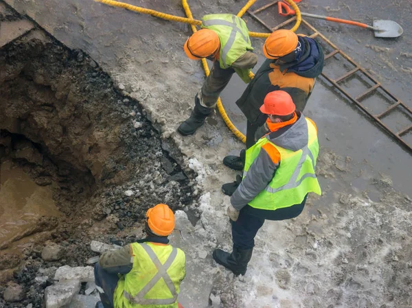A group of road workers from public utilities in reflective special vests are discussing an emergency when digging a hole to eliminate the leakage of pipes in the middle of winter