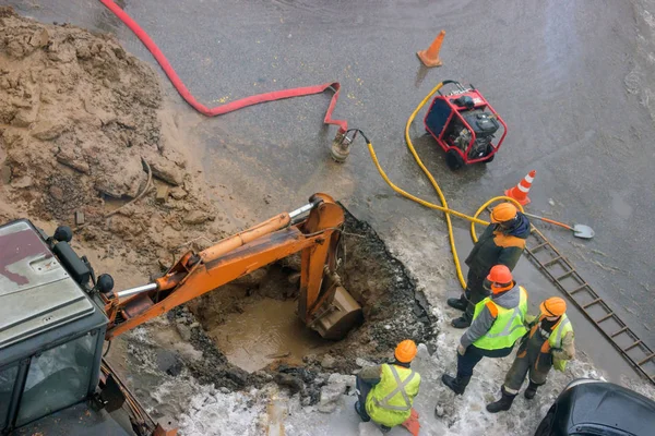 A group of road workers from public utilities in reflective special vests are discussing an emergency when digging a hole to eliminate the leakage of pipes in the middle of winter