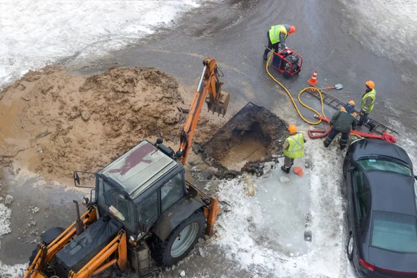 A group of road workers from public utilities in reflective special vests are discussing an emergency when digging a hole to eliminate the leakage of pipes in the middle of winter