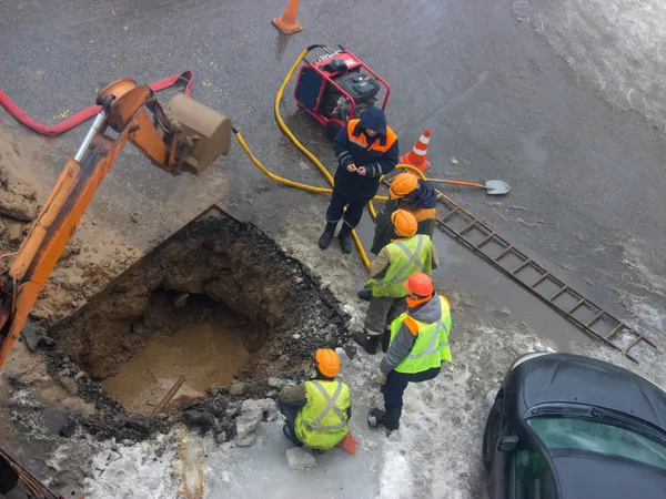 A group of road workers from public utilities in reflective special vests are discussing an emergency when digging a hole to eliminate the leakage of pipes in the middle of winter