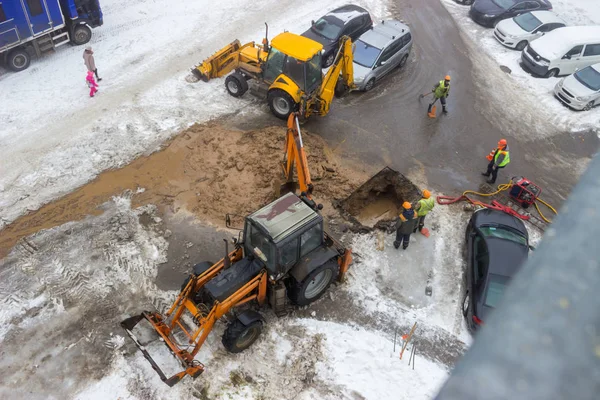 A group of road workers from public utilities in reflective special vests are discussing an emergency when digging a hole to eliminate the leakage of pipes in the middle of winter