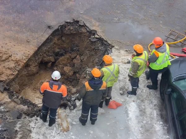 A group of road workers from public utilities in reflective special vests are discussing an emergency when digging a hole to eliminate the leakage of pipes in the middle of winter