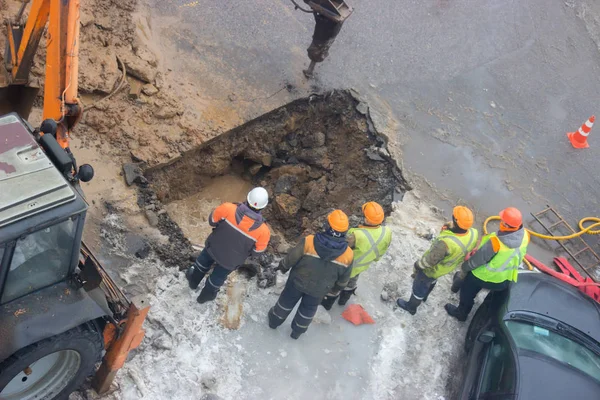 Kışın ortasında borular kaçağı ortadan kaldırmak için bir delik kazma zaman yol işçilerin komün yansıtıcı özel yelekler içinde gelen bir grup acil görüşüyorlar