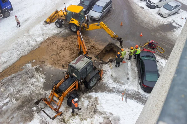 A group of road workers from public utilities in reflective special vests are discussing an emergency when digging a hole to eliminate the leakage of pipes in the middle of winter