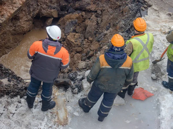 Kışın ortasında borular kaçağı ortadan kaldırmak için bir delik kazma zaman yol işçilerin komün yansıtıcı özel yelekler içinde gelen bir grup acil görüşüyorlar