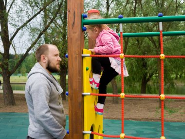 Babası merdiven ve yerel park crossbars tırmanabilir miyim onun küçük bebek kızı, güvenli oyun üzerinde yatay çubuk yanında duruyor.