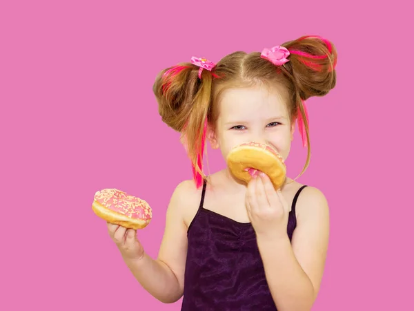 小快乐可爱的女孩正在粉红色的背景墙上吃甜甜圈 孩子们正在和甜甜圈玩得很开心 美味的食物玩孩子 和甜食在一起的时间很有趣 明亮的女婴与粉红色的头发 — 图库照片
