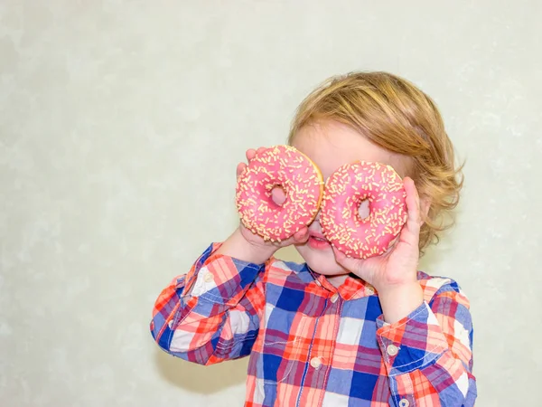 Küçük mutlu sevimli çocuk beyaz arka plan duvar üzerinde donut yiyor. Çocuk eğlenceli poğaça ile geçiriyor. Çocuklar oynamak için lezzetli yemekler. Tatlı gıda ile komik zaman. Ekose gömlekli erkek parlak bebek.