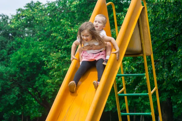 İki çocuk oyun alanı ve heyecan verici bir hızda çığlık sarı slayt aşağı rulo. Çocuk aktif açık parkta gündüz oyun.