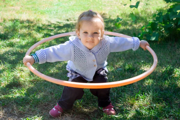 Little baby girl learns to deal with hulahup. The child holds the hoop with two hands. Baby is trying to twist the hoop around the waist. Girl dabbles with a hoop and smiles.