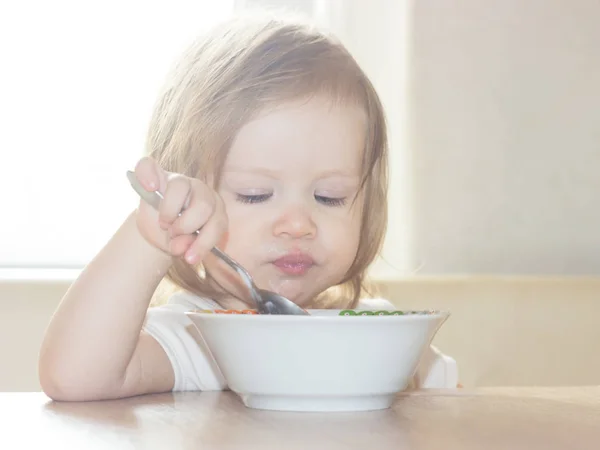 小毛茸茸的女婴与快乐独自拿着勺子 吃美味的食物从一个白色的盘子 — 图库照片