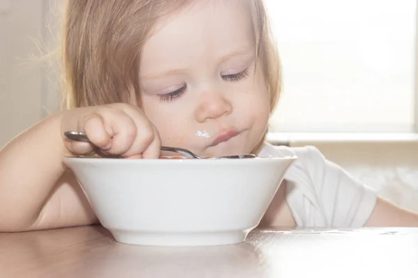 小毛茸茸的女婴与快乐独自拿着勺子 吃美味的食物从一个白色的盘子 — 图库照片