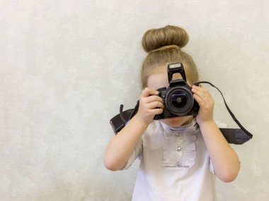 Iş kıyafetleri küçük bir kız onu güzel yüzünün önünde elinde bir refleks kamera tutar. Çocuk fotoğraf çekmek istiyor. Bebek deklanşöre parmağını tutar..