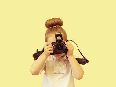 Beyaz elbiseli zeki bir kız yüzünün önünde bir refleks kamera tutar. Çocuk fotoğraf çekmek istiyor. Bebek deklanşöre parmağını tutar..