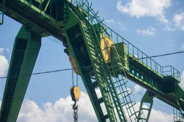 Fragman, gantry yeşil vinç yakın çekim ayrıntıları. Köprü vincinin bir kısmı mavi gökyüzü ve beyaz bulutlara karşı aşağıdan vurulur.