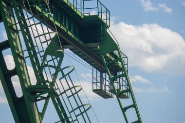 Fragman, gantry yeşil vinç yakın çekim ayrıntıları. Köprü vincinin bir kısmı mavi gökyüzü ve beyaz bulutlara karşı aşağıdan vurulur.