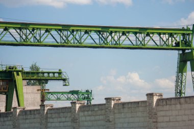 Fragman, gantry yeşil vinç yakın çekim ayrıntıları. Köprü vincinin bir kısmı mavi gökyüzü ve beyaz bulutlara karşı aşağıdan vurulur.