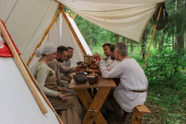 Grodek, Polonya - 13 Temmuz 2019. Erken Ortaçağ hayatında yetişkinler için bir oyun. Tarihi kostümlü insanlar tentenin altında ortaçağ masasında oturuyorlar. Ormandaki stratejik konuların sıcak tartışması.