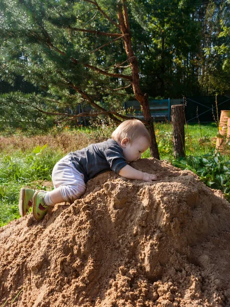 Il ragazzino gioca a King of the Hill su un mucchio di sabbia fresca e bagnata arancione. bambino assaggia la sabbia dalla cima della collina — Foto Stock