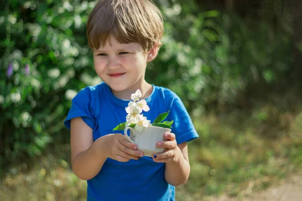 De jongen houdt een boeket jasmijn in een beker. cadeau van zijn zoon voor de vakantie. — Stockfoto