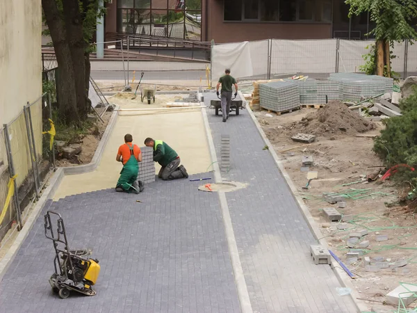 Tres albañiles de trabajo están colocando losas de pavimentación en una plaza de la ciudad reconstruida . — Foto de Stock