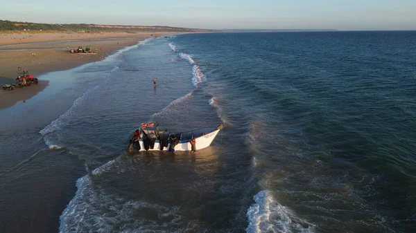 Costa da Caparica, Portekiz 22 Ağustos 2025: Balıkçıların teknelerini okyanus dalgalarına sürdükleri hava manzarası. Sahilde geleneksel balıkçılık sahnesi, takım çalışması ve deniz yaşamı yukarıdan ele geçirildi.