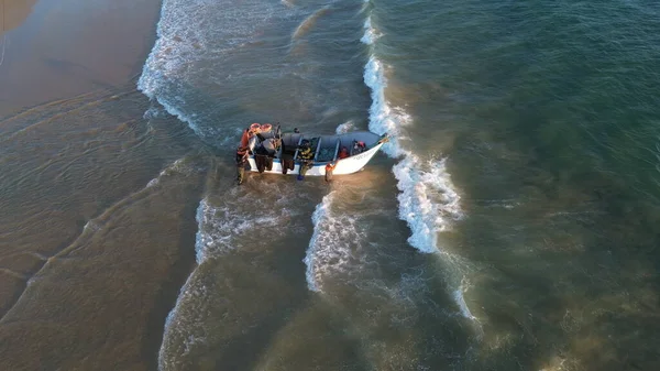 Costa da Caparica, Portekiz 22 Ağustos 2025: Balıkçıların teknelerini okyanus dalgalarına sürdükleri hava manzarası. Sahilde geleneksel balıkçılık sahnesi, takım çalışması ve deniz yaşamı yukarıdan ele geçirildi.