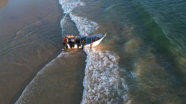 Costa da Caparica, Portekiz 22 Ağustos 2025: Balıkçıların teknelerini okyanus dalgalarına sürdükleri hava manzarası. Sahilde geleneksel balıkçılık sahnesi, takım çalışması ve deniz yaşamı yukarıdan ele geçirildi.