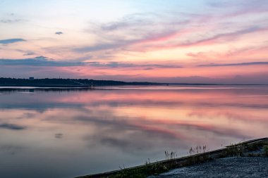 Nehrin üzerinde pembe gün batımı, su deposu, deniz. Ufukta orman görünüyor. Yatay yönelim. 